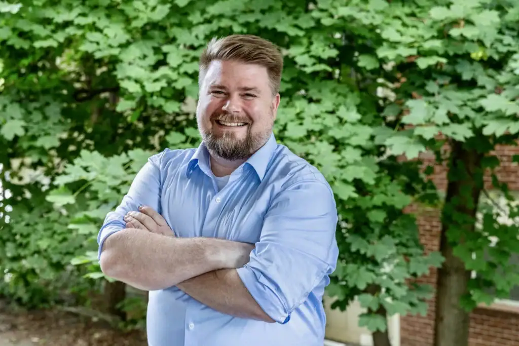 Olivia Therrien smiling outdoors in front of green foliage.