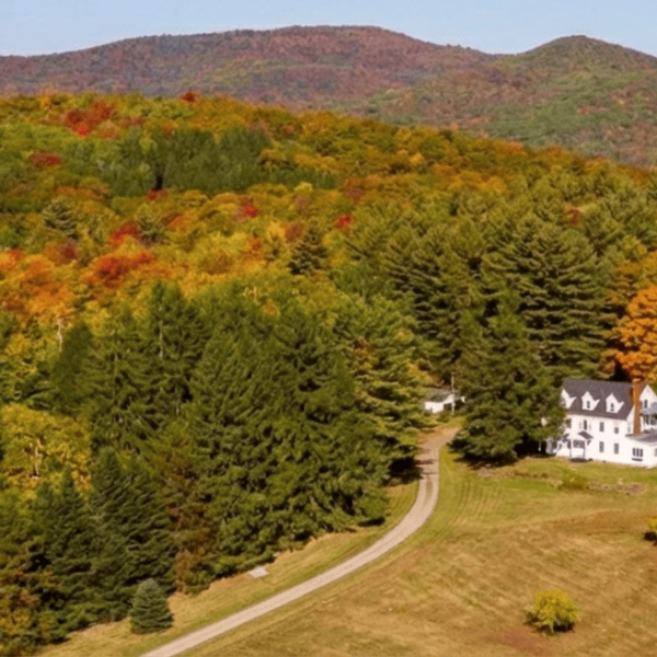 Aerial view of a house surrounded by colorful fall foliage in a forested mountain area.