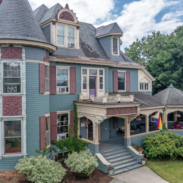Victorian transitional living house with porch and lush greenery.