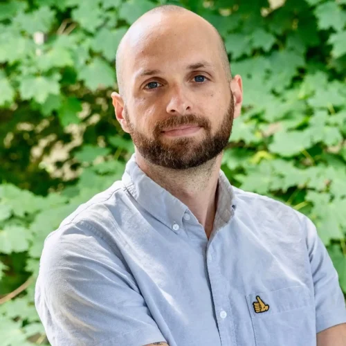 Olivia Therrien smiling outdoors with green foliage background.