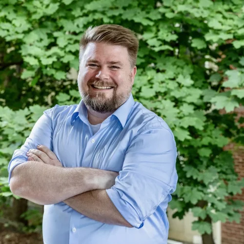 Olivia Therrien smiling outdoors in front of green foliage.