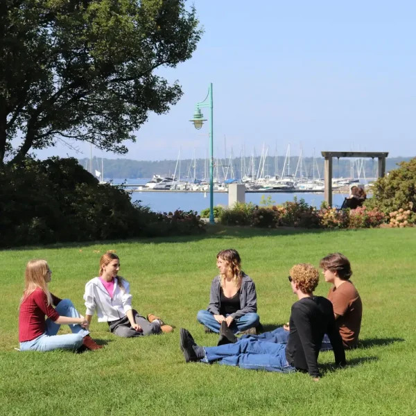 Group of young adults sitting on grass near waterfront in transitional living program.
